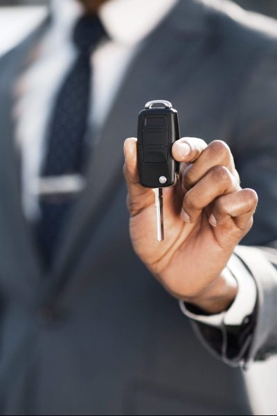 New car owner. Businessman showing car key against luxury auto, copy space